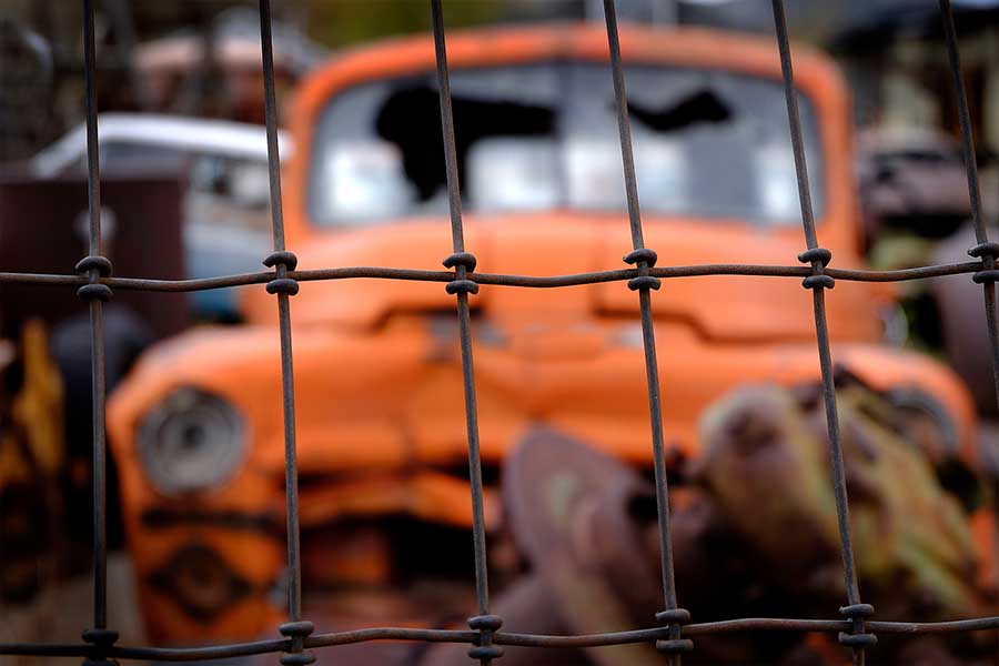 Junked truck behind a junkyard fence